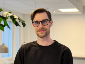Porträtt av August Viberg. Han har kort brunt hår och har på sig glasögon och en svart tjocktröja.